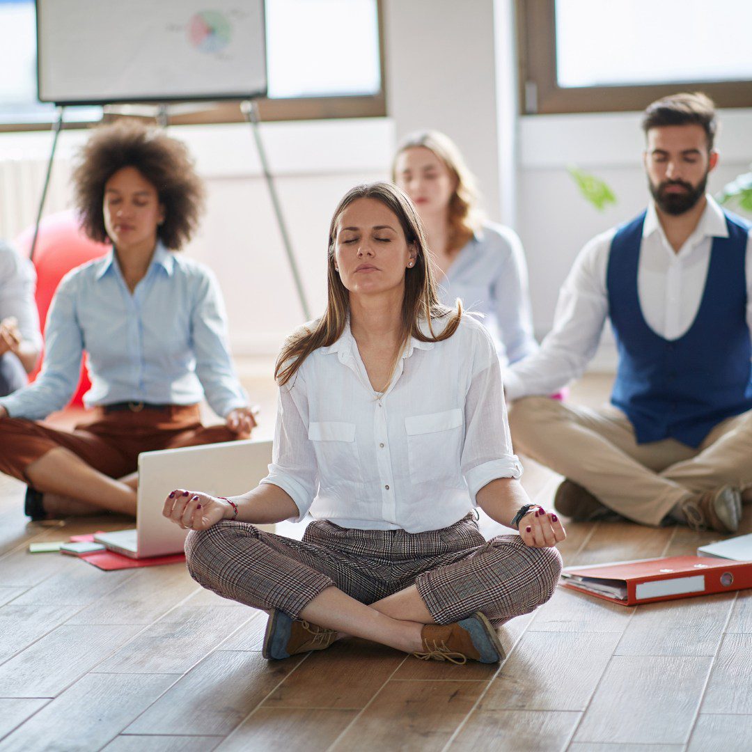 A group of people sitting in the middle of an office yoga class.