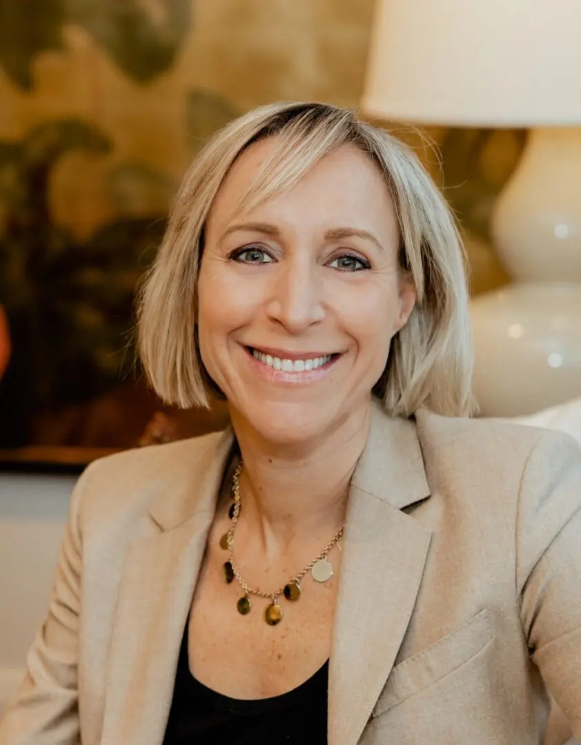 A woman with blonde hair and wearing a beige jacket.