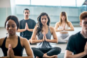 A group of people sitting in the middle of a yoga class.